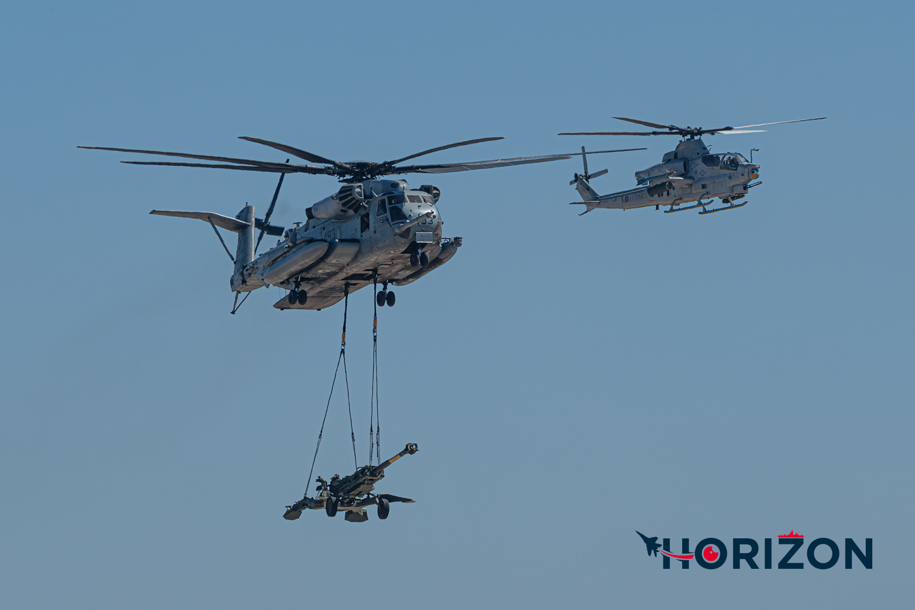 US Marine Corps CH-53E Super Stallion carrying an M777 Howitzer artillery cannon alongside a Bell AH-1Z Viper.